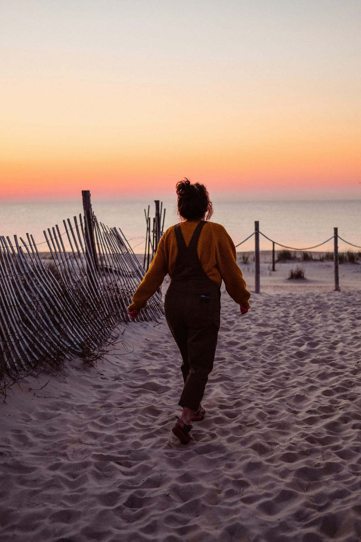 A woman seen from behind walking along a sandy beach path at sunset