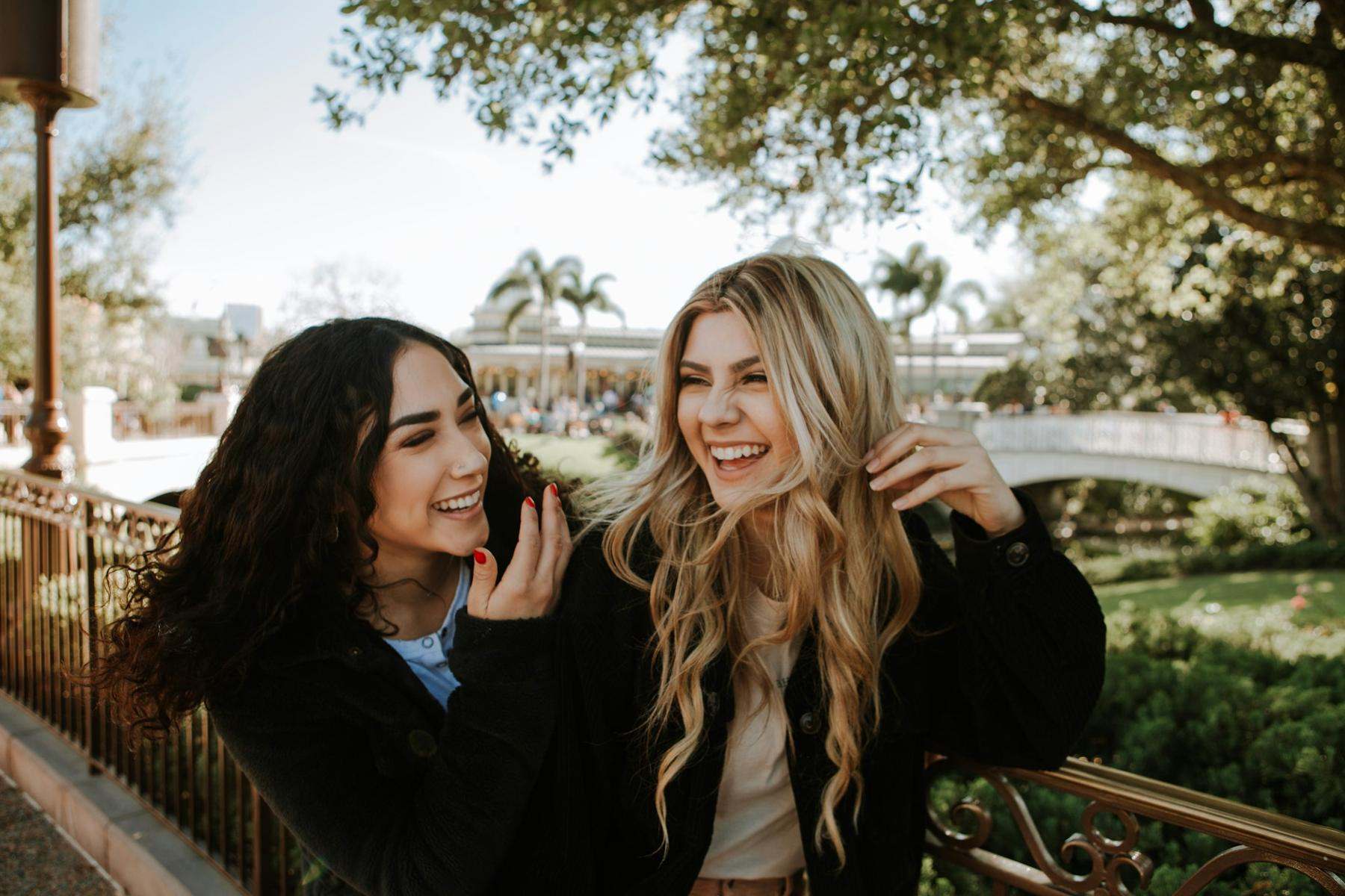 Two friends laughing together outdoors on a sunny day