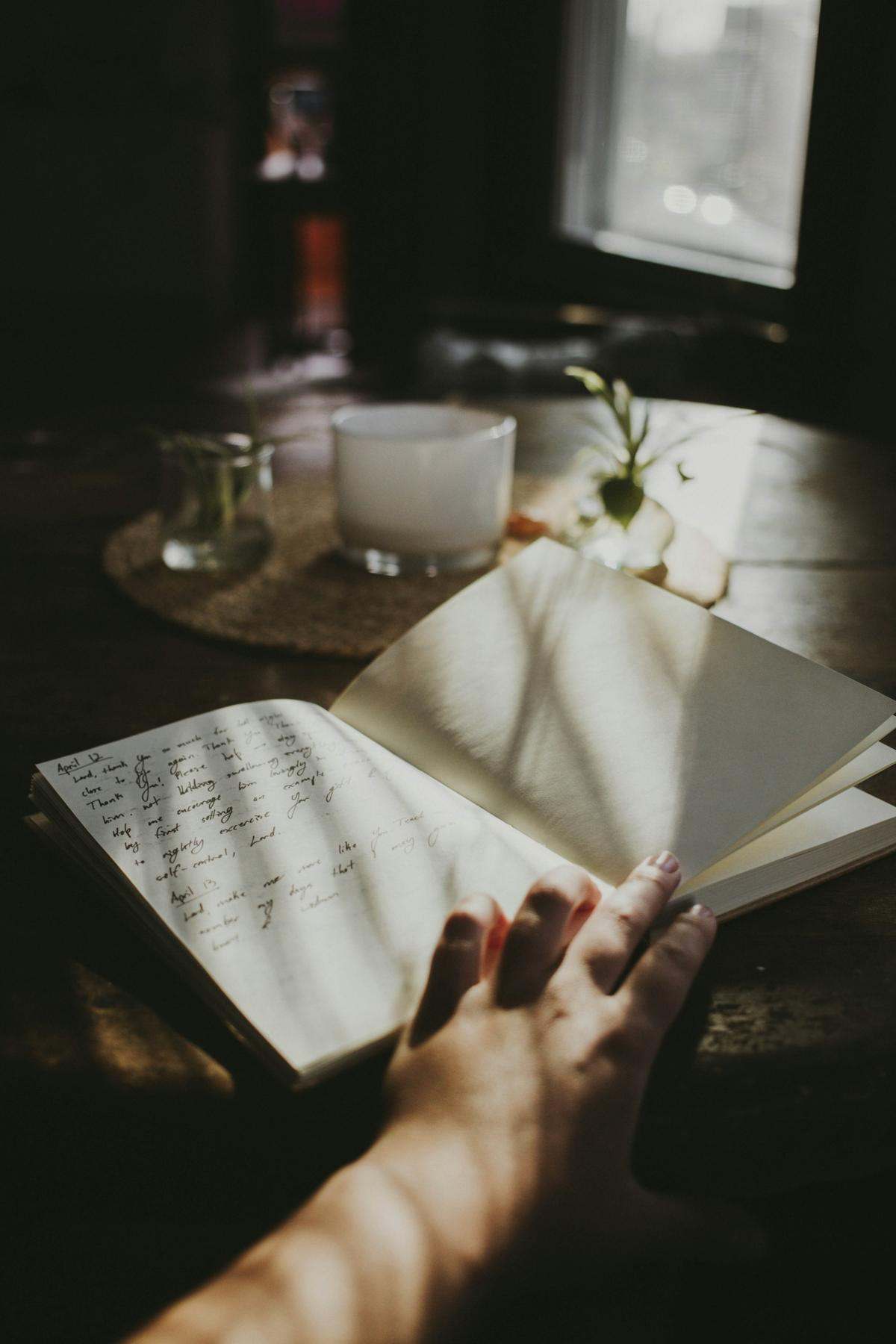 A hand turning the pages of a handwritten notebook on a table