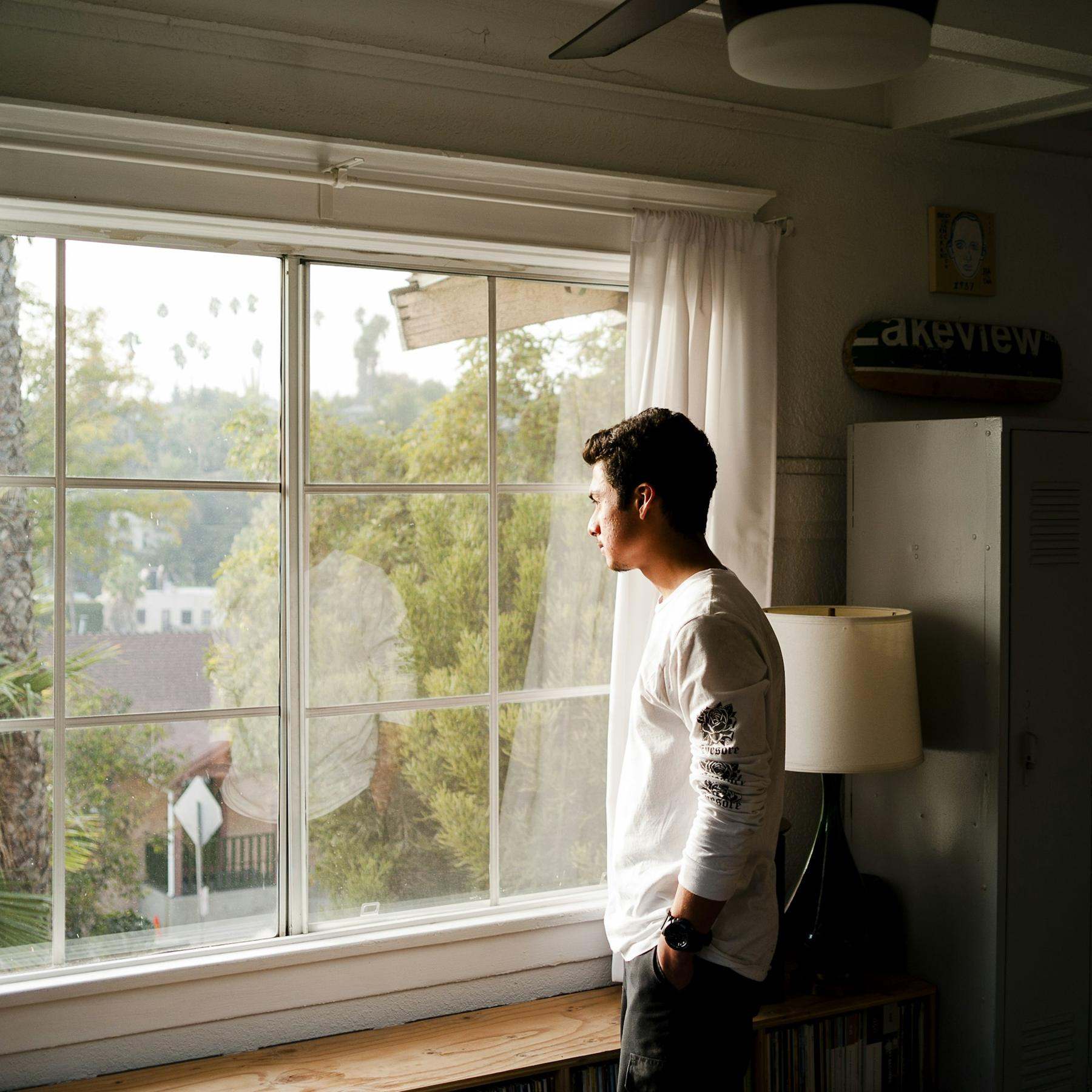 A young man in a white top looking out of a large window