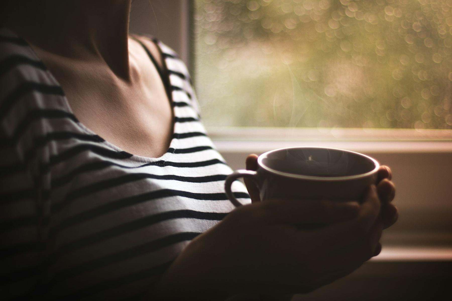 Hands holding a mug of tea by a window