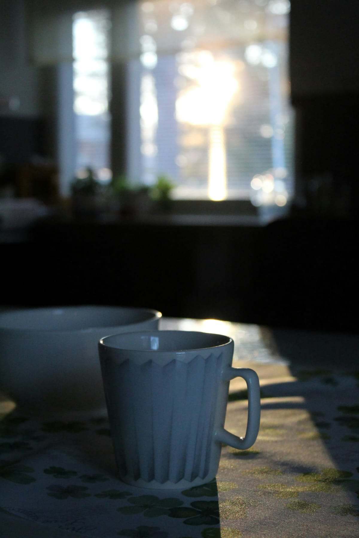 A white mug on a kitchen table with morning sun through the window